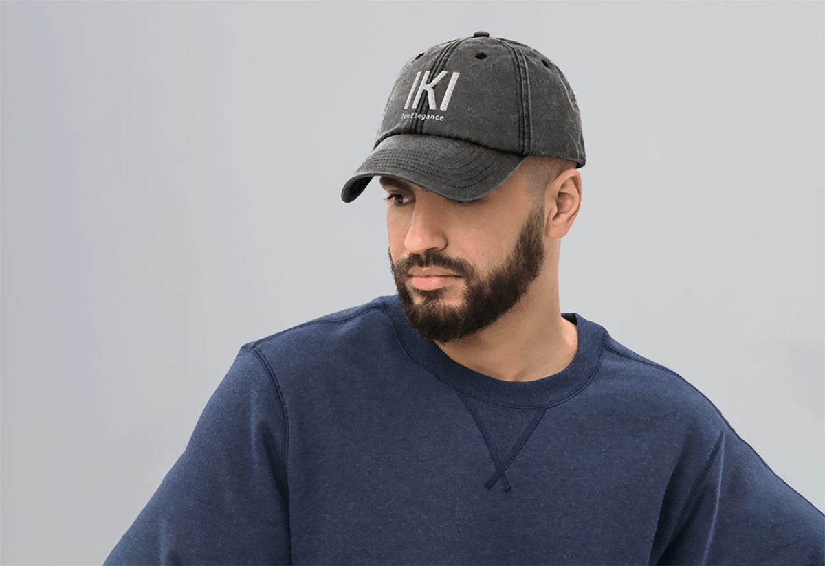 Modelo con jersey azul marino y gorra IKI negro lavado contra una pared clara